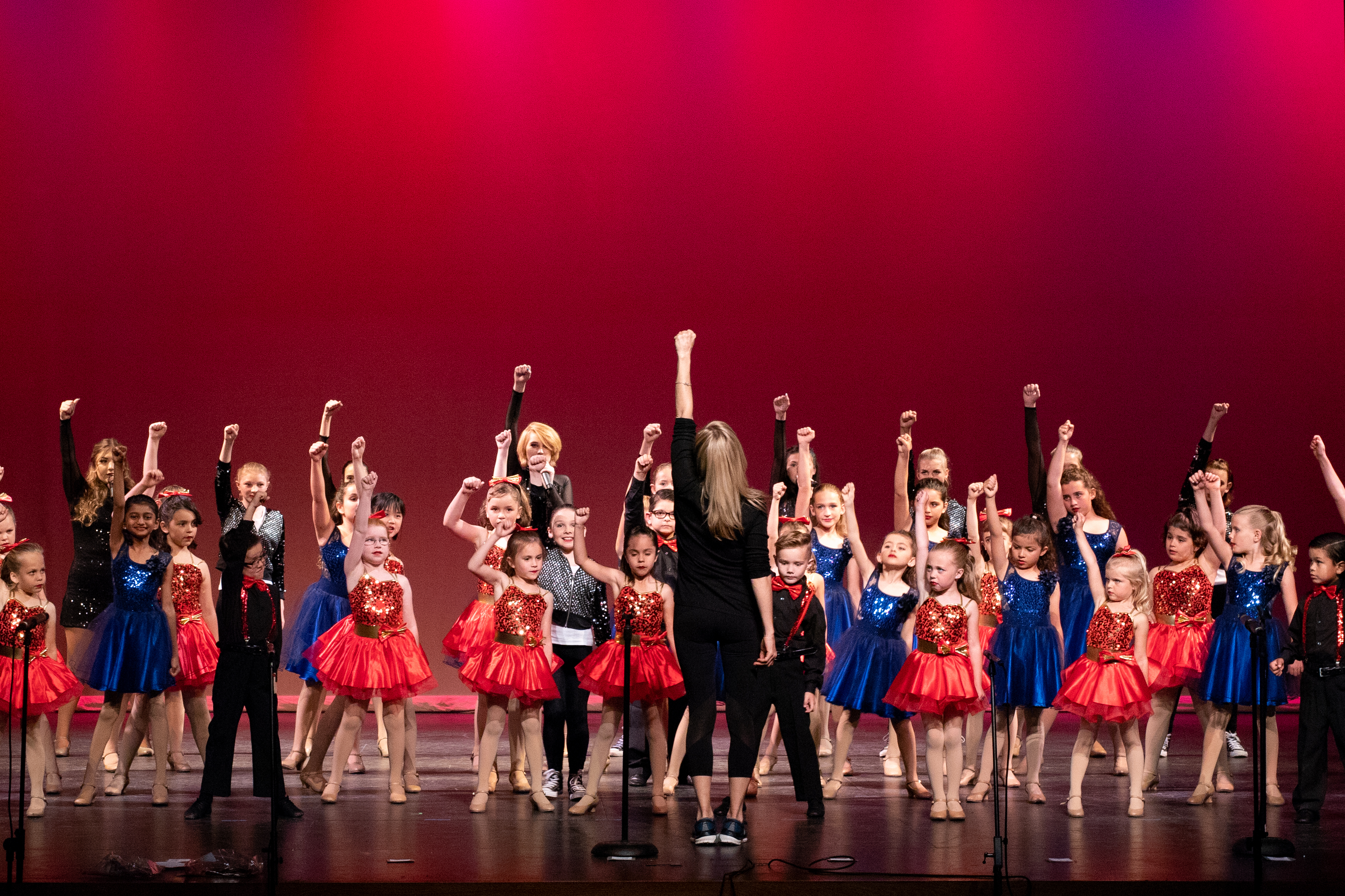 Children and adults performing a lively dance on stage with raised fists.