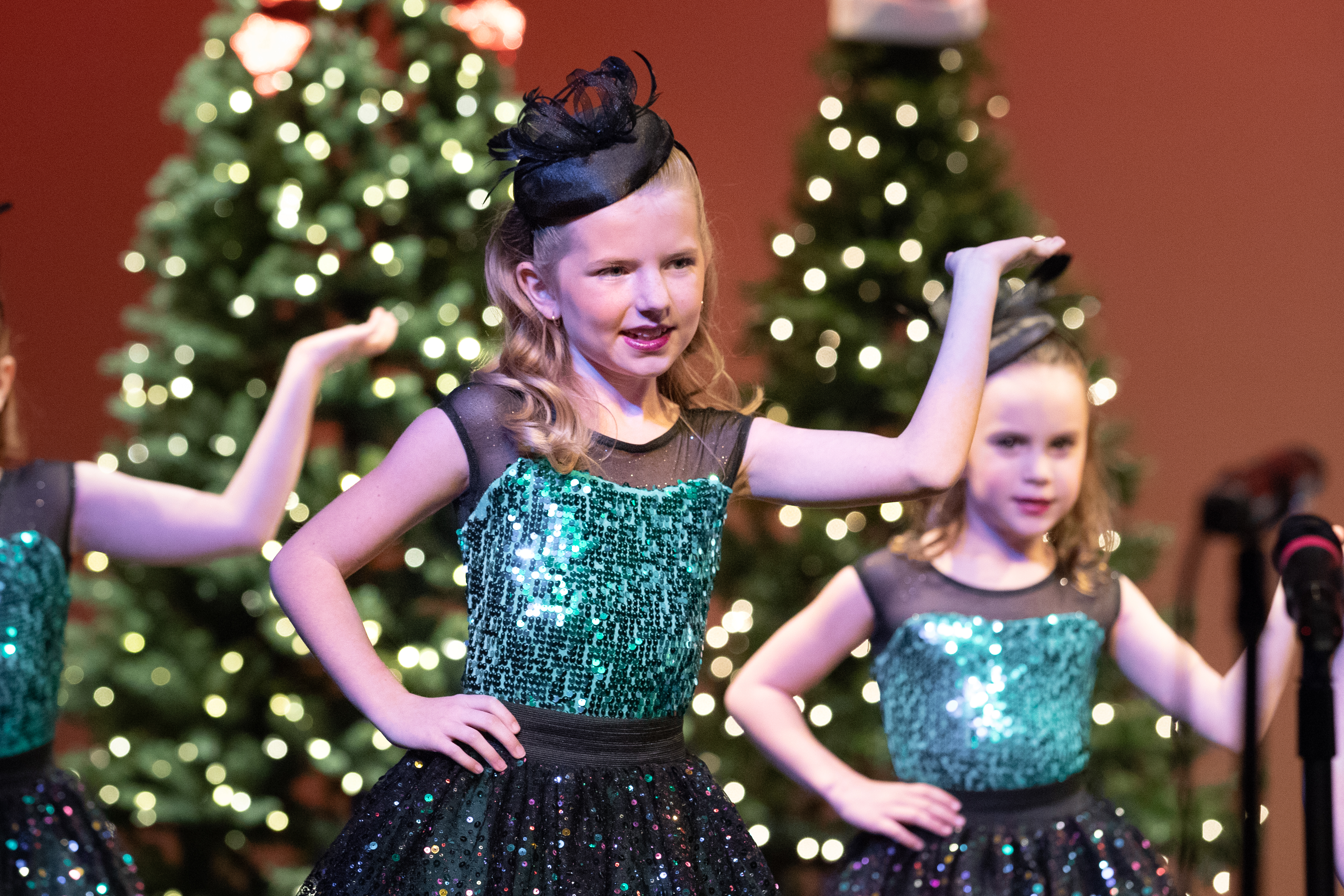 Young girls performing on stage in sparkly green and black costumes.