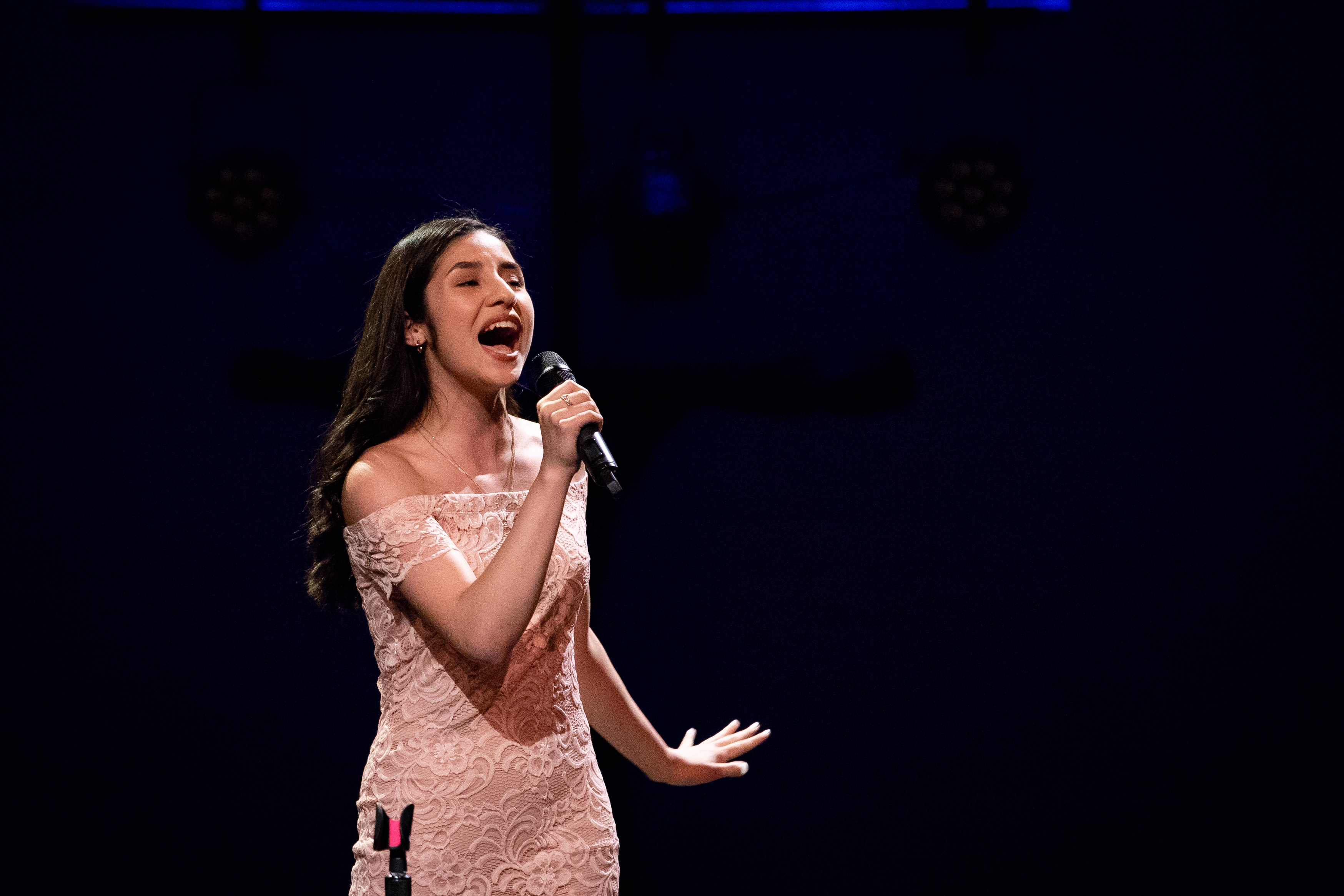 A woman passionately singing on stage in a sparkling dress.
